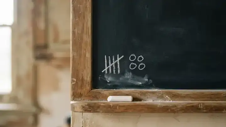A wooden-framed chalk slate with a small chalk tally of lines and circles in the corner, light moving slowly across it